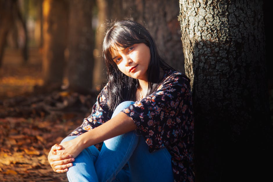 Un retrato sereno de una mujer joven sentada en un bosque otoñal iluminado por el sol, capturando la tranquilidad de la naturaleza.